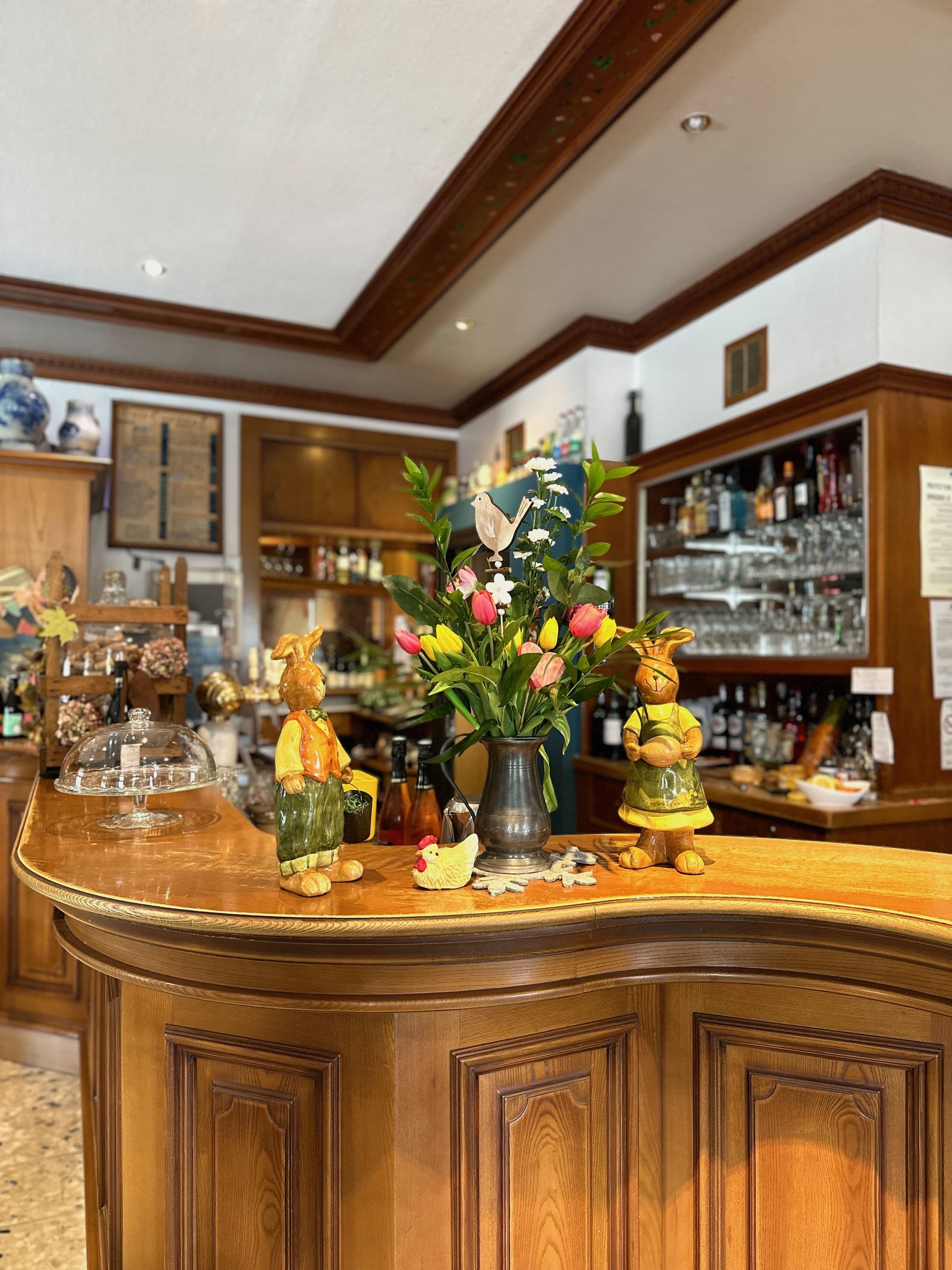 Comptoir en bois chaleureux du bar-restaurant décoré de tulipes colorées et de figurines en céramique, avec verres et bouteilles en arrière-plan.