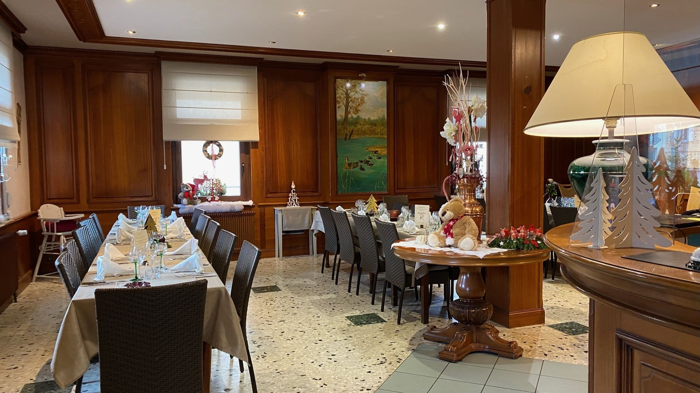 Salle à manger traditionnelle à panneaux de bois avec longues tables dressées pour un repas festif, décorations de Noël et centre de table en peluche, créant une atmosphère chaleureuse et familiale.