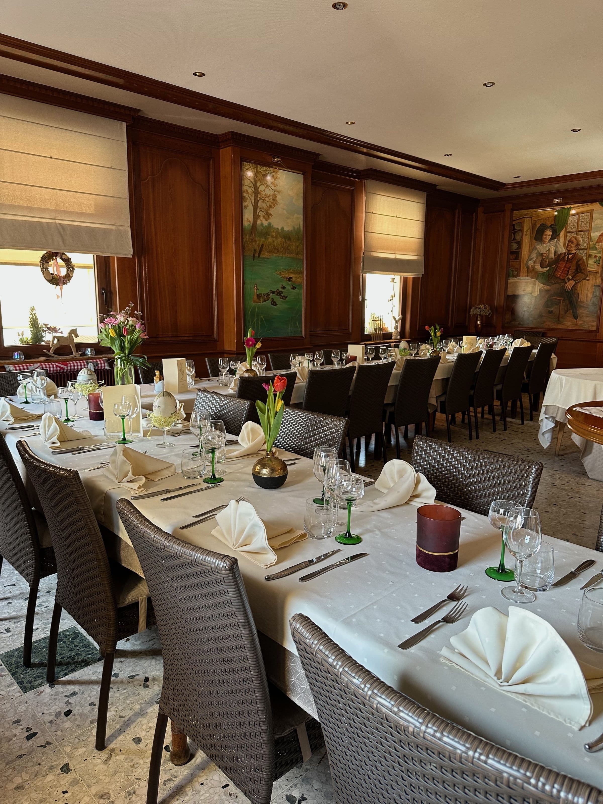 Salle à manger traditionnelle alsacienne chaleureusement éclairée avec longues tables dressées, chaises en osier et boiseries murales.